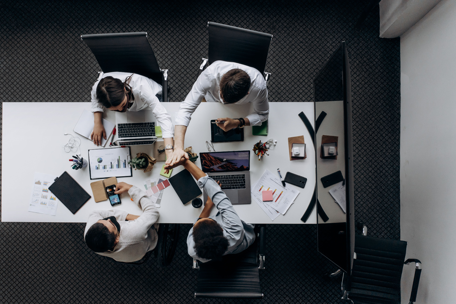 Team collaborating around a conference table, hands joined in commitment
